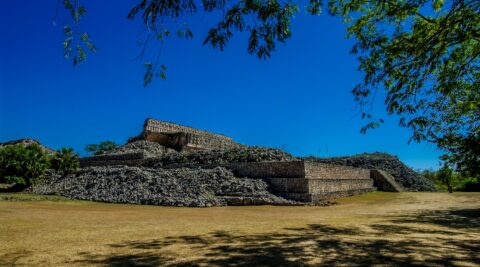 Standing In The Shadow And Look From The Distance At Mayan Building In Kabah Archaeological Site In Yucatan, Mexico